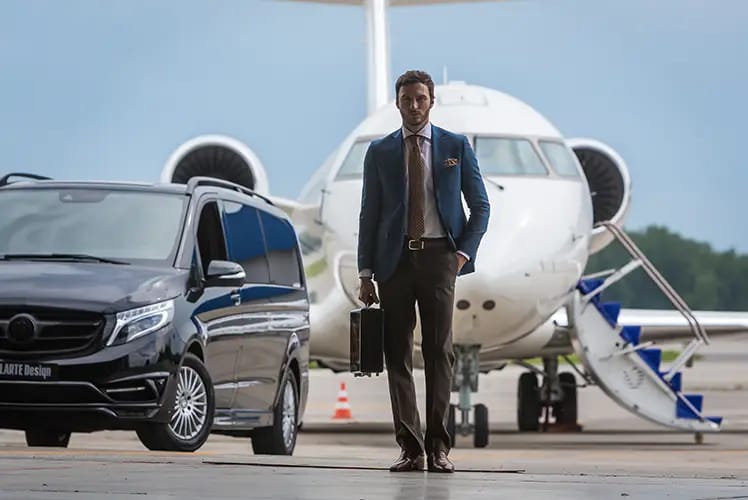 A well-dressed man stands next to a sleek car and a private jet-condor security Executive Protection Toronto